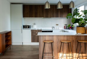 A modern kitchen with wooden cabinets, a central island with stools, pendant lighting, and a large plant. - Beautiful rural cottage in a tranquil East Lothian countryside setting (Haddington)
