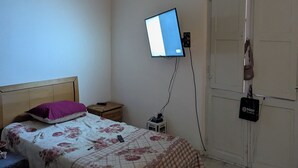 Ett sovrum med en säng, en tv som är monterad på väggen, en garderob och ett litet nattduksbord.