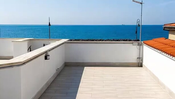 A rooftop terrace with a view of the sea, a metal railing, and a tiled floor. - Vacation House Grecale Apartment Leonardo Airport (Isola Sacra)