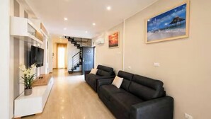 A modern living room with a sofa, a flat-screen TV, and a staircase leading to another level. - Vacation House Grecale Apartment Leonardo Airport (Isola Sacra)