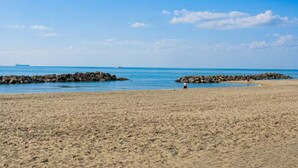 A sandy beach with rocky outcrops, a clear blue sky, and a distant ship. - Vacation House Grecale Apartment Leonardo Airport (Isola Sacra)