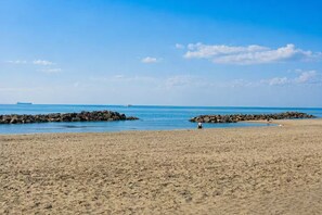Una playa arenosa con afloramientos rocosos, un cielo azul despejado y un barco a lo lejos.