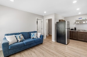 A modern apartment with a blue sofa, a black refrigerator, wooden flooring, and a kitchen area.