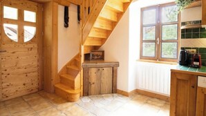 Een houten trap die uitkomt op een plateau, een houten deur met raam, en een keuken met raam en aanrecht.