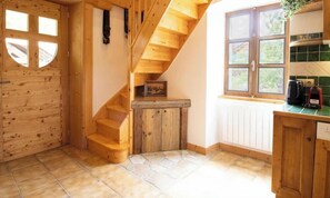 A wooden staircase leading to a landing, a wooden door with a window, and a kitchen area with a window and a countertop.