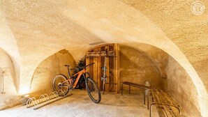 Een gewelfde stenen kamer met een fiets, een houten deur en een bank.