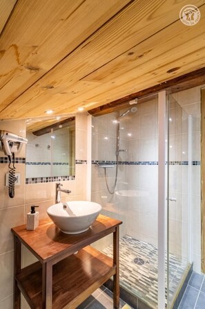 Techo de madera, lavamanos blanco, cabina de ducha de vidrio y suelo de baldosas.