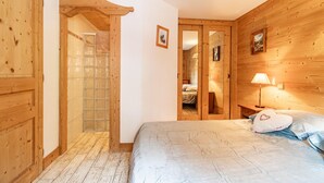 Een kamer met houten lambrisering, een bed, een nachtkastje en een deur die naar een andere ruimte leidt.