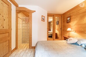 Habitació amb panells de fusta, un llit, una tauleta de nit i una porta que condueix a una altra habitació.