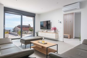 Ein modernes Wohnzimmer mit einer Couch, einem Couchtisch, einem Fernseher und Blick ins Freie.