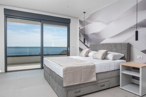 Ein Schlafzimmer mit Bett, Nachttisch, einer eingebauten Ablage, einer großen Schiebeglaswand und Meerblick.