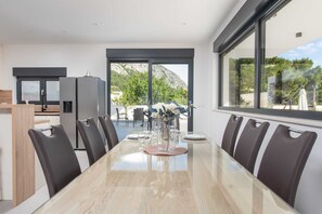 Ein moderner Essraum mit einem langen Tisch, schwarzen Stühlen und großen Fenstern mit Blick ins Freie.