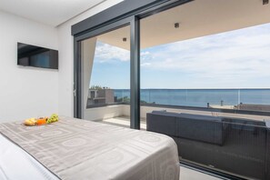 Ein modernes Schlafzimmer mit Bett, einem kleinen Tisch mit Obst und einem Balkon mit Meerblick.