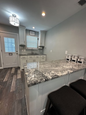 A kitchen with a granite countertop, white cabinets, a window with blinds, and a ceiling light fixture.