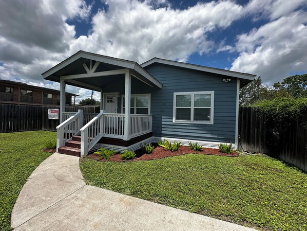A two-story house with a front porch, a small front yard, and a wooden fence.