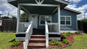 A single-story house with a front porch, a door, and a small front yard with plants.