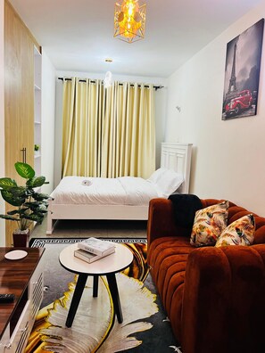 Une chambre à coucher avec un lit, un canapé, une petite table, une plante en pot et un tableau représentant la Tour Eiffel.