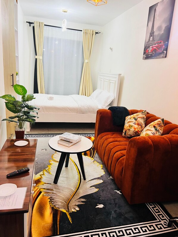 Ein Hotelzimmer mit einem Bett, einer Couch, einem Esstisch, einer Topfpflanze und einem Gemälde vom Eiffelturm.