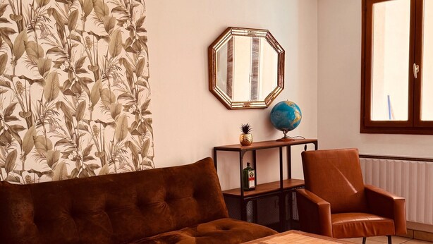 Una sala de estar con un sofá marrón, una mesa de centro de madera, un papel tapiz estampado, un globo terráqueo y una lámpara colgante.