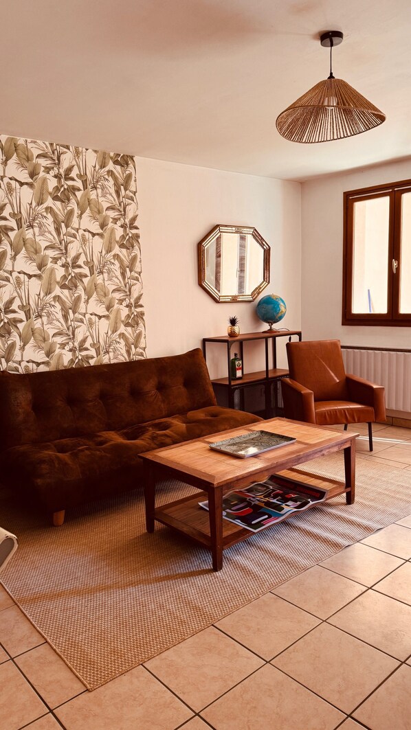 Un salon avec un canapé marron, une table basse en bois, un mur à motifs, un globe terrestre et un luminaire suspendu.