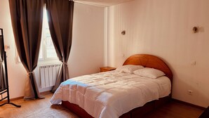Un dormitorio con cama de madera, mesita de noche, radiador y ventana con cortinas.