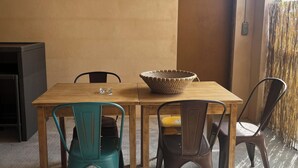 Una mesa de comedor con sillas, una cesta y una puerta en una habitación con suelo de concreto y paredes lisas.