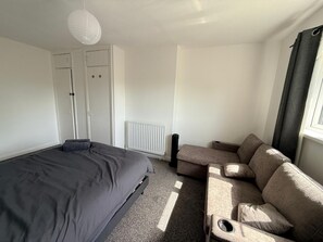 Un dormitorio con cama, sofá, radiador y ventana con cortinas.