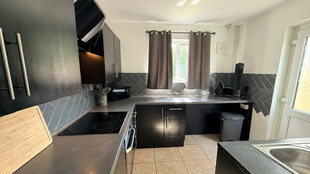A compact kitchen with a stove, microwave, and sink, a small window with curtains, and a door with a light fixture. -  Semi-Detached w/Pool Table & Garden (Cardiff)