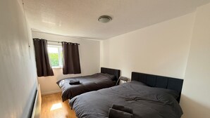 A bedroom with two beds, a window with curtains, a radiator, and a ceiling light. -  Semi-Detached w/Pool Table & Garden (Cardiff)