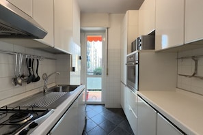A narrow kitchen with white cabinets, a stainless steel stove, and a view through a glass door. - 5 Minuten zu Fuß vom Bahnhof Milano Lambrate (Milan)
