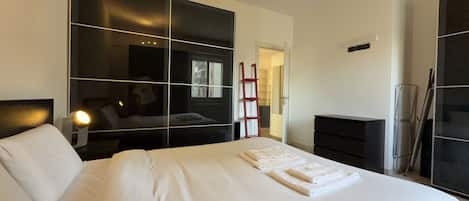 A modern hotel room with a large bed, a wardrobe, a desk, and a mirror.