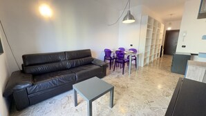 A modern living room with a black leather sofa, a small grey table, purple chairs, a white shelving unit, and a hanging light fixture. - 5 Minuten zu Fuß vom Bahnhof Milano Lambrate (Milan)