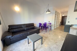 A modern living room with a black leather sofa, a small grey table, purple chairs, a white shelving unit, and a hanging light fixture. - 5 Minuten zu Fuß vom Bahnhof Milano Lambrate (Milan)