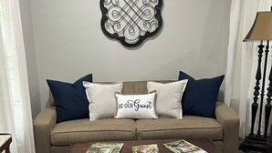 Een woonkamer met een bank, twee kussens, een bijzettafeltje en een decoratief wandobject.
