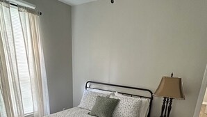 Een slaapkamer met een bed, nachtkastje, lamp en een raam met gordijnen.