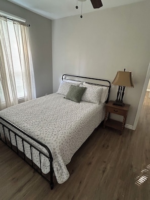 A bedroom with a bed, a nightstand, a lamp, and a window with curtains.
