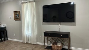 Een woonkamer met een flatscreen-televisie aan de muur, een console met lades en een rieten mandje erop.