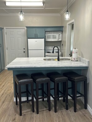 A kitchen with a large island, bar stools, a microwave, and a refrigerator. - The Julep House - a 2-bedroom cottage in Beautiful Saint Francisville, LA! (Saint Francisville)