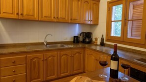 A kitchen with wooden cabinets, a sink, a coffee maker, a wine bottle, and glasses on the counter. - Casa Ramón, rural retreat by Garajonay Park (Agulo)