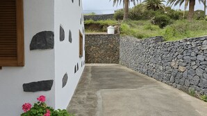 Un bâtiment blanc aux murs de pierre, un chemin en béton et des plantes en pot.