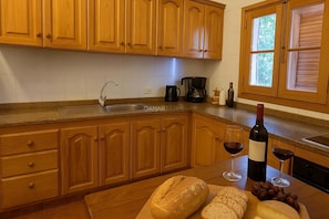 Una cocina con armarios de madera, un fregadero, una cafetera, una botella de vino y vasos sobre la encimera.