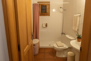 Un baño con ducha, inodoro, lavabo y una pequeña ventana sobre el inodoro.