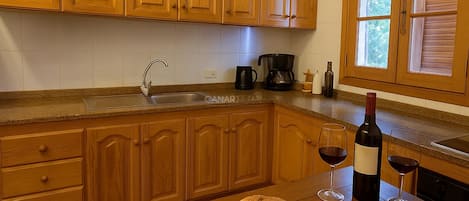 A kitchen with wooden cabinets, a sink, a coffee maker, a wine bottle, and glasses on the counter.