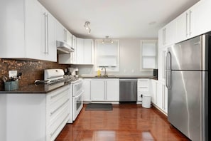 A modern kitchen with white cabinets, stainless steel appliances, and a wooden backsplash. - Modern Comfort in Olde Walkerville (Windsor)