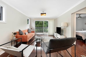 A modern living room with a sofa, armchair, TV, and balcony view. - Modern Comfort in Olde Walkerville (Windsor)