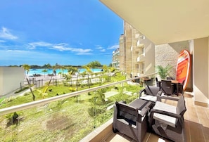 A balcony with wicker furniture overlooking a pool and greenery. - Kristal lagoon apartment baia cristal (Bolívar)