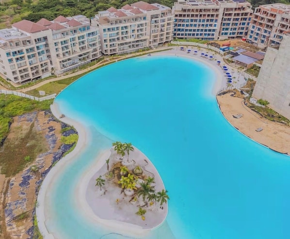 A large, curved swimming pool surrounded by multi-story hotel buildings. - Kristal lagoon apartment baia cristal (Bolívar)