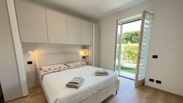 Ein Schlafzimmer mit einem Bett, Nachttischlampen, einem Kleiderschrank und einer Schiebetür zum Balkon.