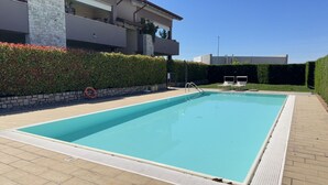 Ein rechteckiger Pool mit weißer Sicherheitsumrandung, einer Steinmauer und einem Hecken.