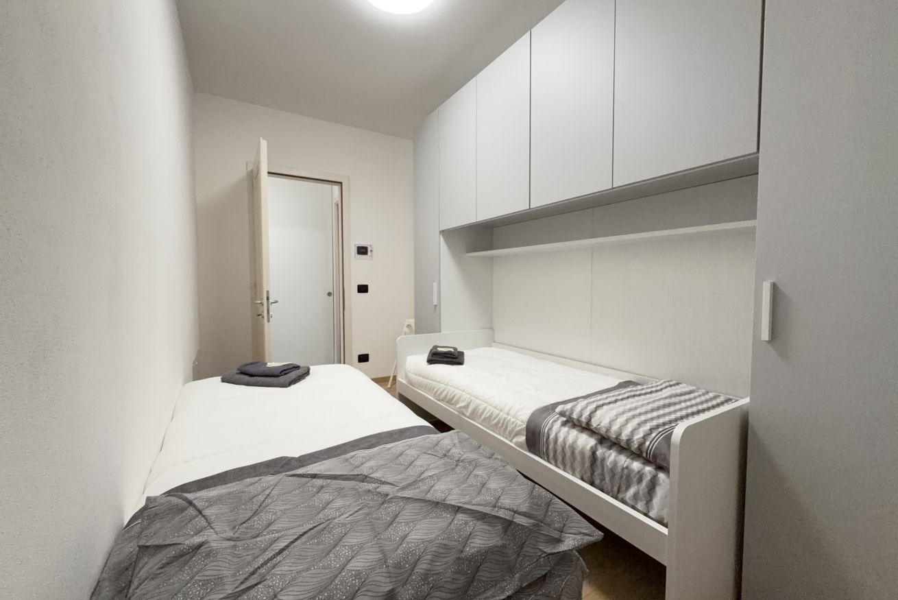 Una habitación pequeña y funcional con una cama individual, un banco y un armario.